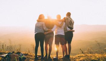Group of young friends huddles while watching a sunset over a valley