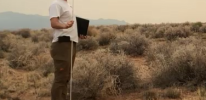 person standing in a desert shrub environment holding a rod.